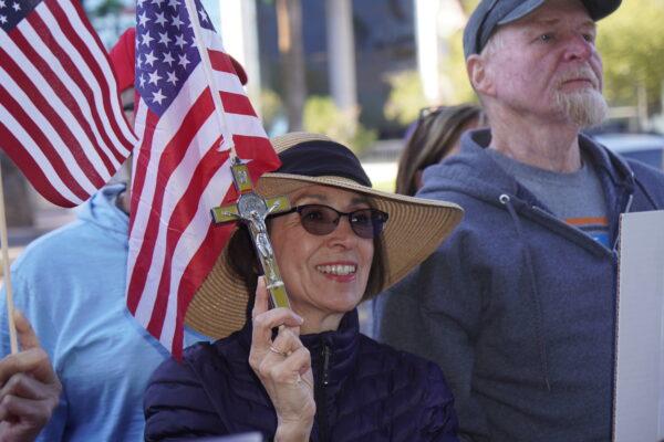 A woman holds a flag and crucifix at an Election Integrity Rally outside the office building of Arizona Attorney General Mark Brnovich on Dec. 17, 2021. (Allan Stein/The Epoch Times)