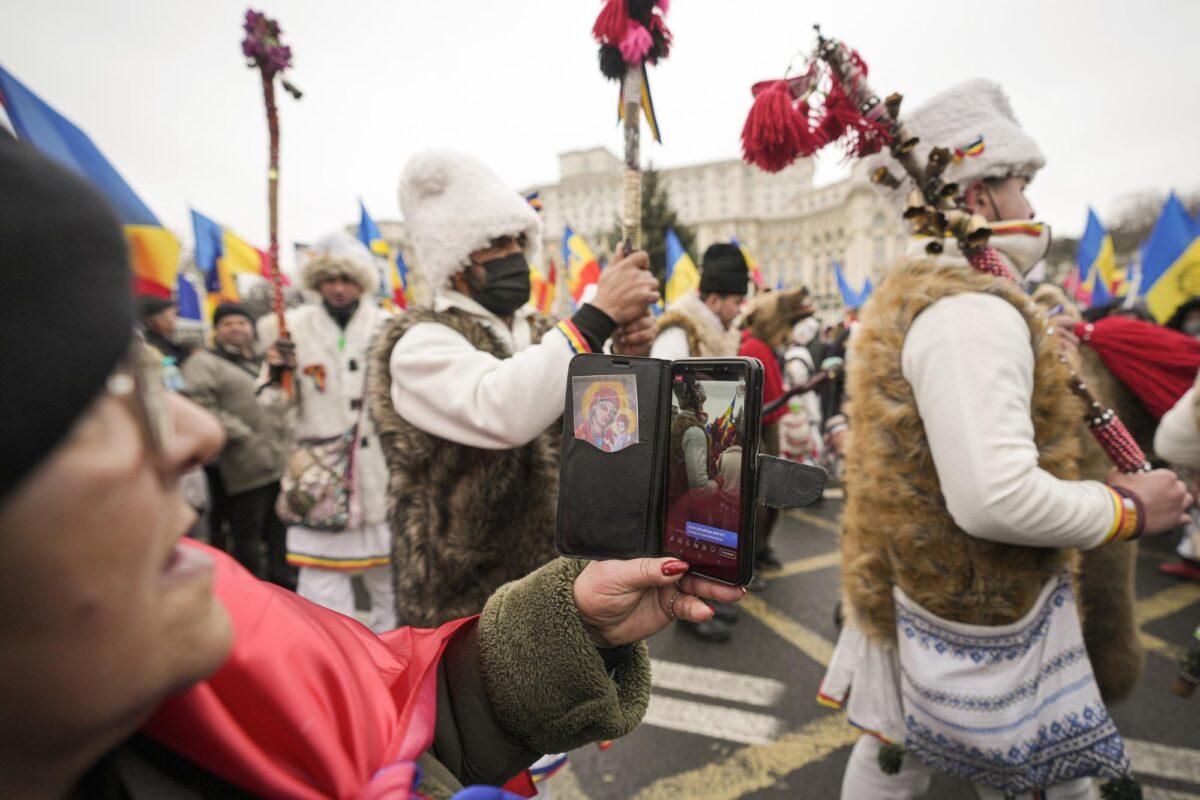 A woman broadcasts a live feed on her mobile phone as Romanians protesting COVID-19 restrictions gather outside the Palace of Parliament in Bucharest, on Dec. 21, 2021. (Vadim Ghirda/AP Photo)