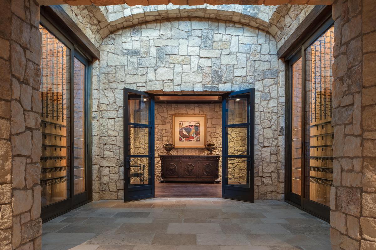 Beneath the entry foyer, a wine gallery leads to the entrance to what is best described as a “wine cave,” given the immensity of the estate’s cellar. Again, the generous use of stone and warm wood exude a sense of welcoming. (Matthew Walla/Jade Mills)