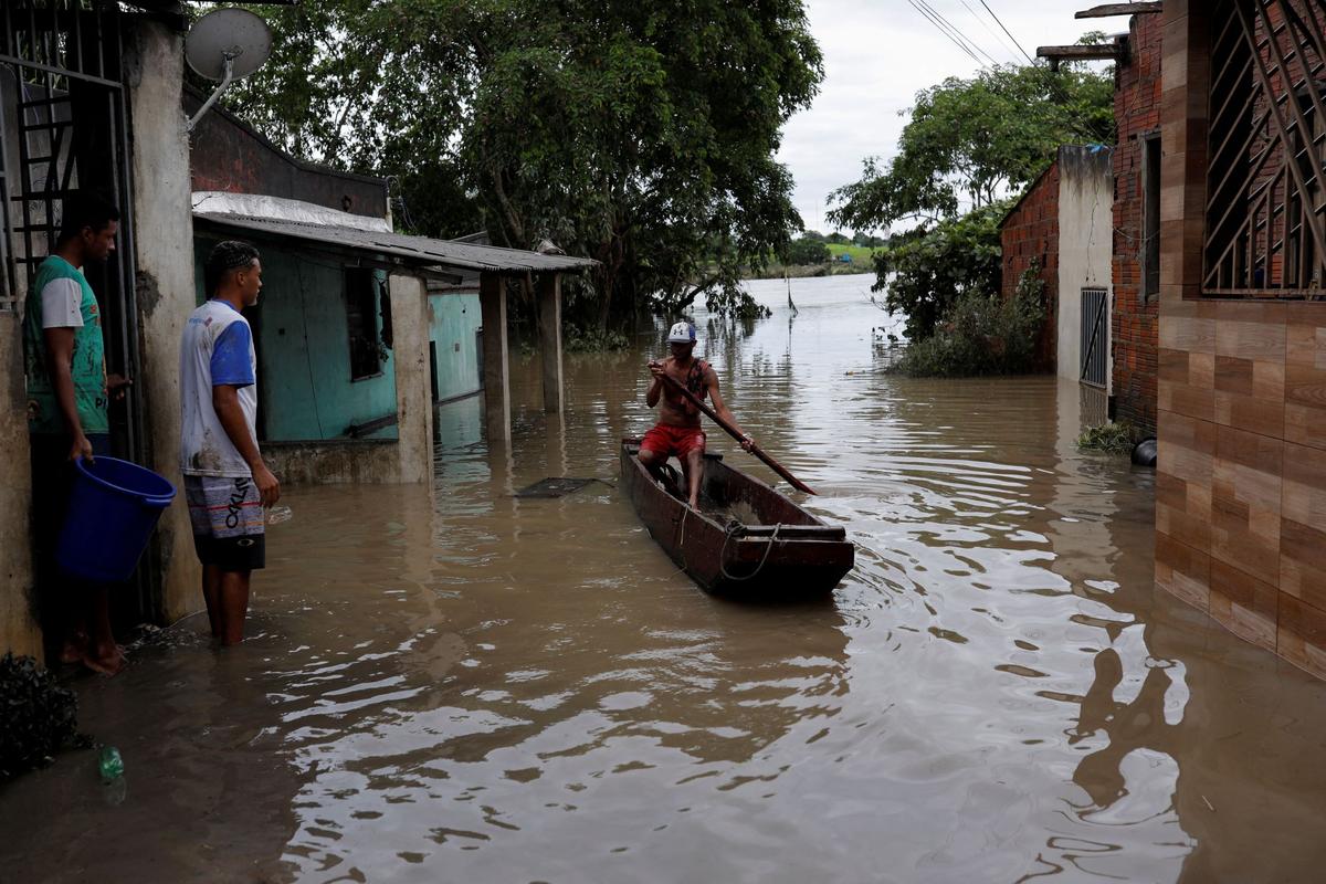 A man paddles a canoe along a street, during floods caused due to heavy rains, in Itabuna, Bahia state, Brazil, on Dec. 27, 2021. (Amanda Perobelli/Reuters)