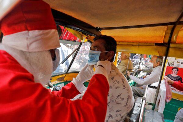 A man wearing a Santa Claus costume adjusts an auto-rickshaw driver's mask as he distributes free masks during the ongoing COVID-19 pandemic, in Ahmedabad, India, on Dec. 24, 2021. (Amit Dave/Reuters)