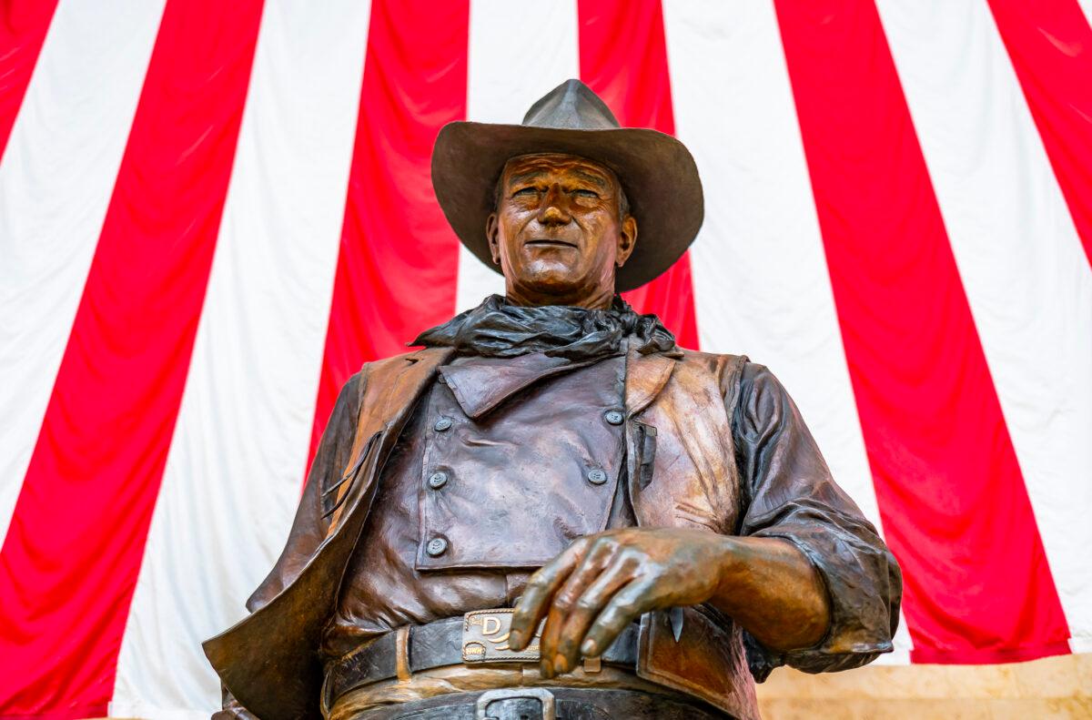 An American flag hangs behind a statue of John Wayne at John Wayne Airport in Santa Ana, Calif. on June 30, 2021. (John Fredricks/The Epoch Times)