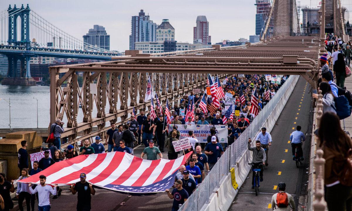 Municipal workers hold placards and shout slogans as they march across Brooklyn Bridge during a protest against the COVID-19 vaccine mandate, in New York on Oct. 25, 2021. (Ed Jones/AFP via Getty Images)