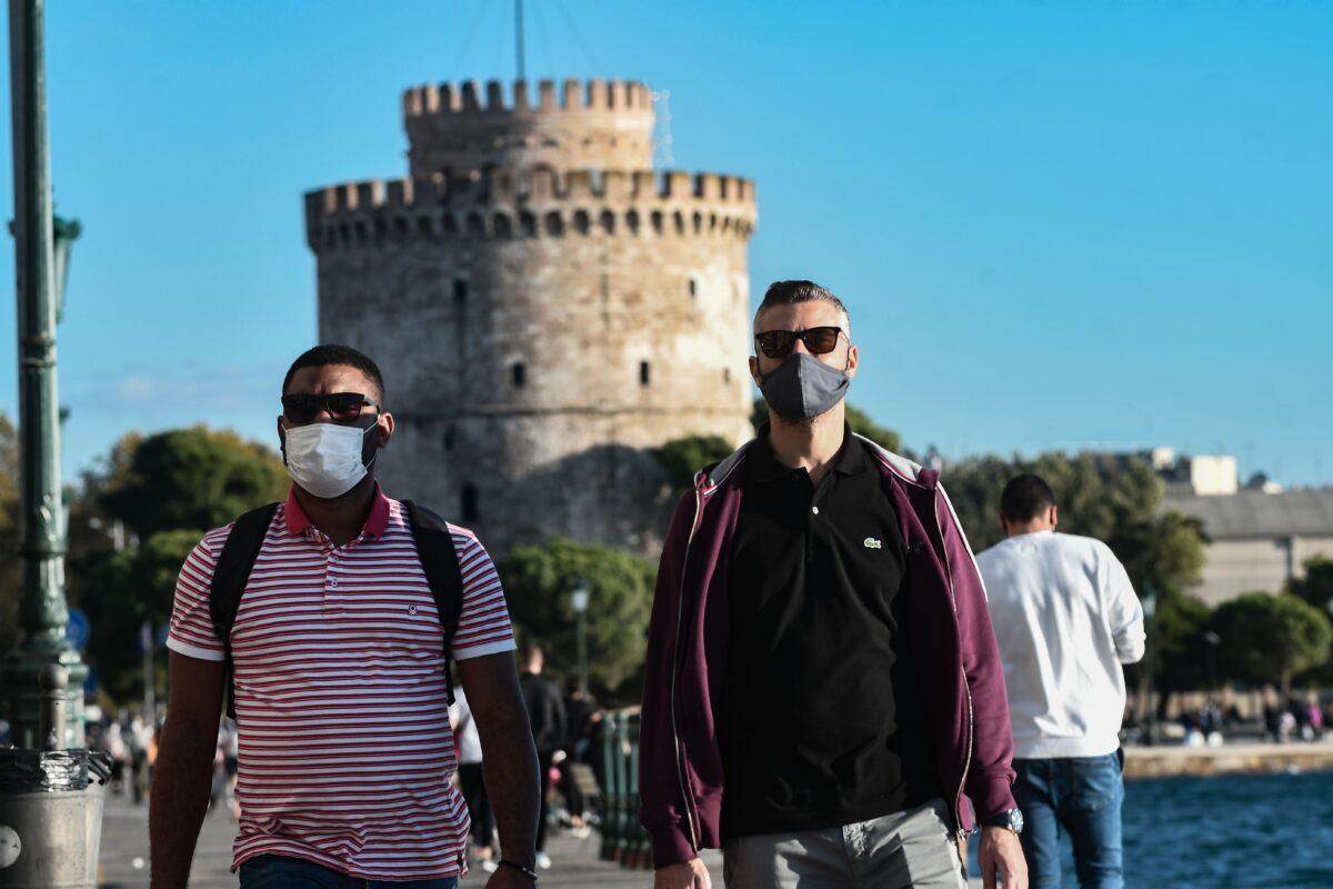 Pedestrians, wearing protective face masks, walk on the waterfront next to the White Tower in Thessaloniki, Greece, on Oct. 31, 2020. (Sakis Mitrolidis/AFP via Getty Images)