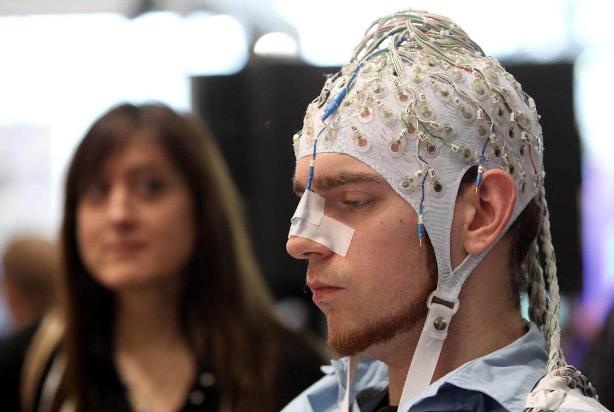 A young woman watches a man, wearing an EEG brain scanning apparatus on his head, play a pinball game solely through willing the paddles to react with his brain at the Berlin Brain Computer Interface research consortium stand at the CeBIT Technology Fair in Hannover, Germany, on March 2, 2010. (Sean Gallup/Getty Images)