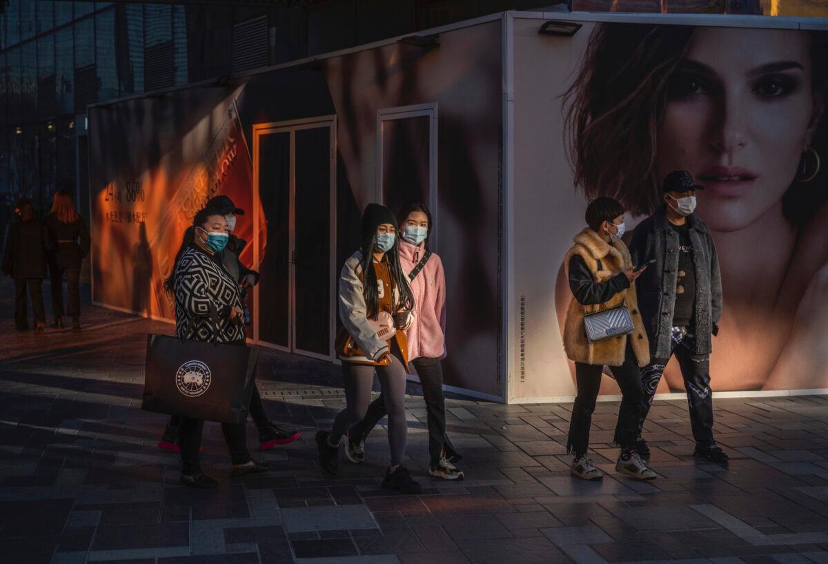 People wear protective masks as they walk by an ad for French luxury fashion brand DIOR outside a new location set to open at a shopping area in Beijing, China, on Nov. 24, 2021. (Kevin Frayer/Getty Images)