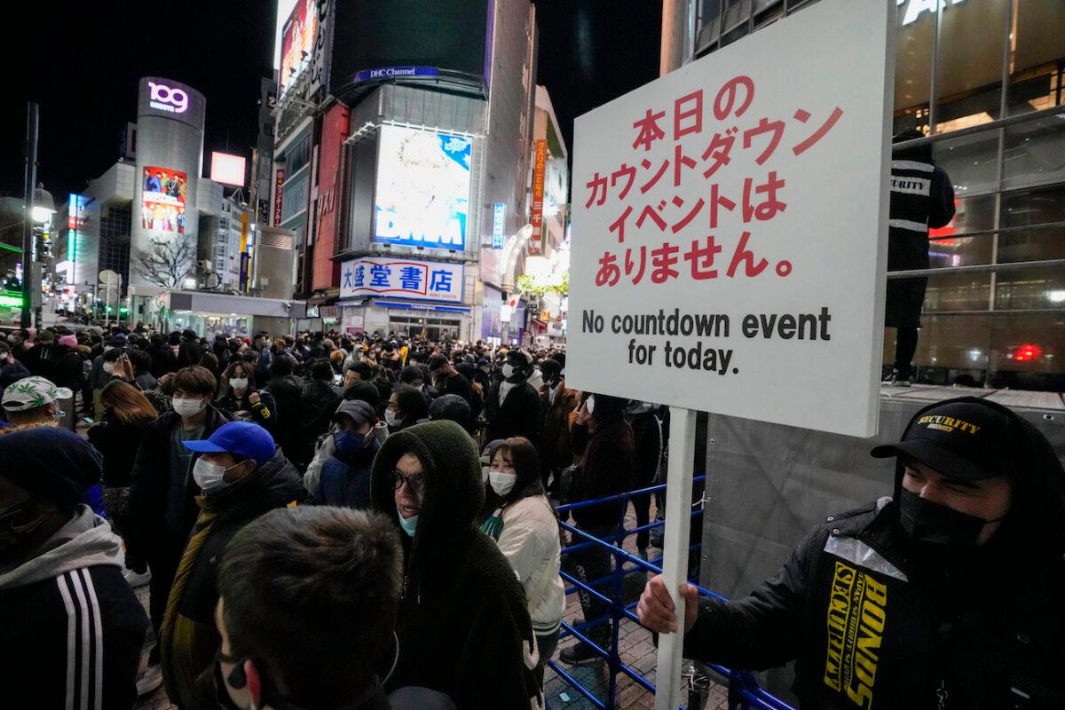 A security guard holds up a sign indicating that there is no countdown event at the famed Shibuya scramble crossing, a popular location for New Year’s Eve gathering, in Tokyo as people gather to celebrate New Year’s eve on Dec. 31, 2021. (Kiichiro Sato/AP Photo)