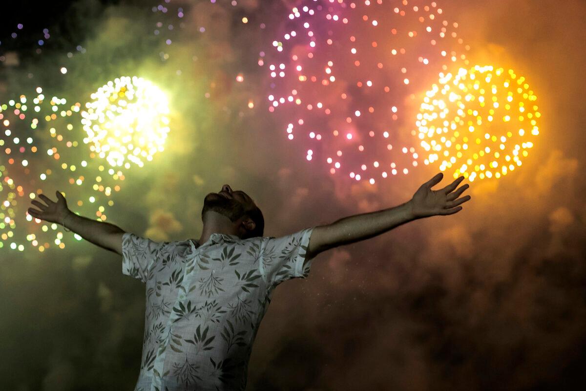 A man celebrates the start of the New Year, backdropped by fireworks exploding in the background over Copacabana Beach in Rio de Janeiro, Brazil, on Jan. 1, 2022. (Bruna Prado/AP Photo)