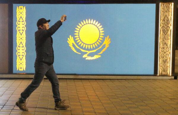 A man holds a mobile phone while walking past a board with a Kazakh state flag during a protest against LPG cost rise following authorities' decision to lift price caps on liquefied petroleum gas in Almaty, Kazakhstan, on Jan. 5, 2022. (Pavel Mikheyev/Reuters)
