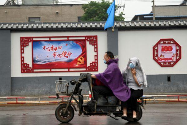 A couple rides past a propaganda mural that reads "Do not forget the original aspirations, keep the mission in mind" on a street in Beijing, China on June 9, 2021. (Noel Celis/AFP via Getty Images)