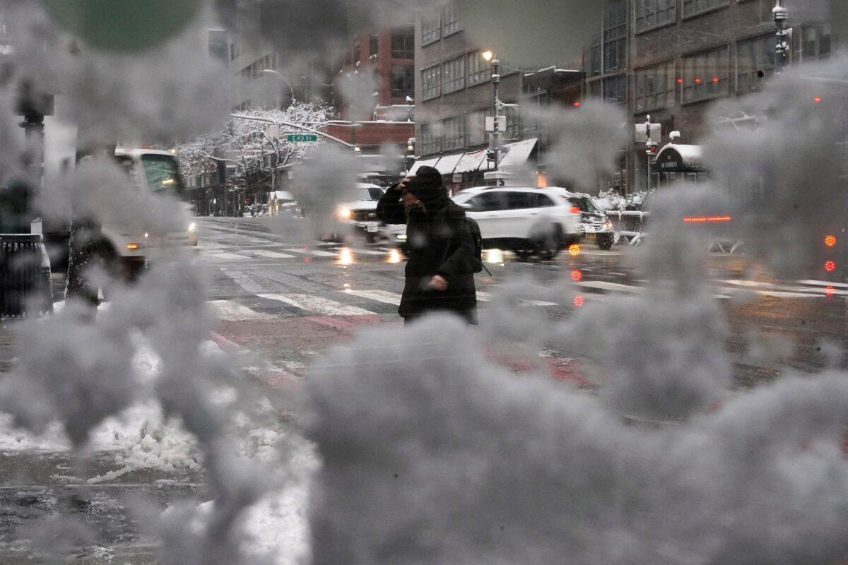 People cross the street through a bus stop window in the snow in the Manhattan borough of New York City on Jan. 7, 2022. (Carlo Allegri/Reuters)