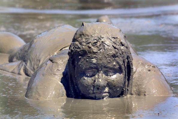 WESTLAND, MI - JULY 8: Natasha McDaniels, 12, of Westland, Michigan lays in the mud during the annual Mud Day celebration July 8, 2003 in Westland, Michigan. Hundreds of children and teens participate in the event which allows them to play in a lake of mud made from several hundred thousand gallons of water and dirt. (Photo by Bill Pugliano/Getty Images)