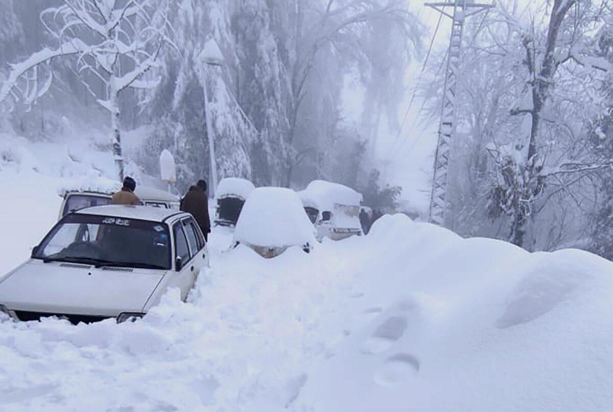 In this photo provided by the Inter-Services Public Relations, people walk past vehicles trapped in a heavy snowfall-hit area in Murree, Pakistan, on Jan. 8, 2022. (Inter-Services Public Relations via AP)