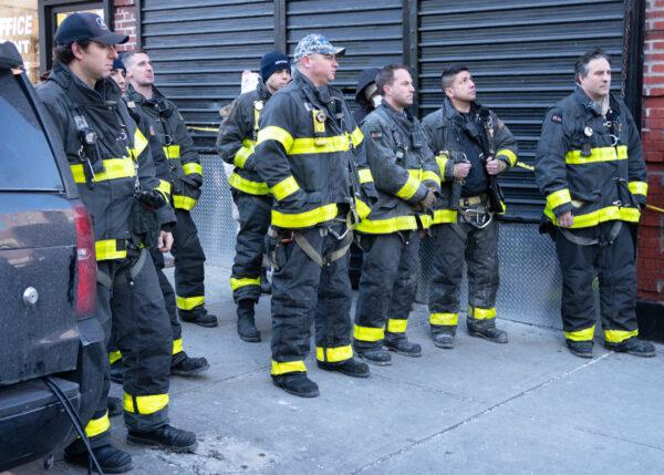 New York City firefighters watch the press conference in the Bronx, New York, at the site of a five-alarm, apartment building fire on Jan. 10, 2022. (Dave Paone/The Epoch Times)
