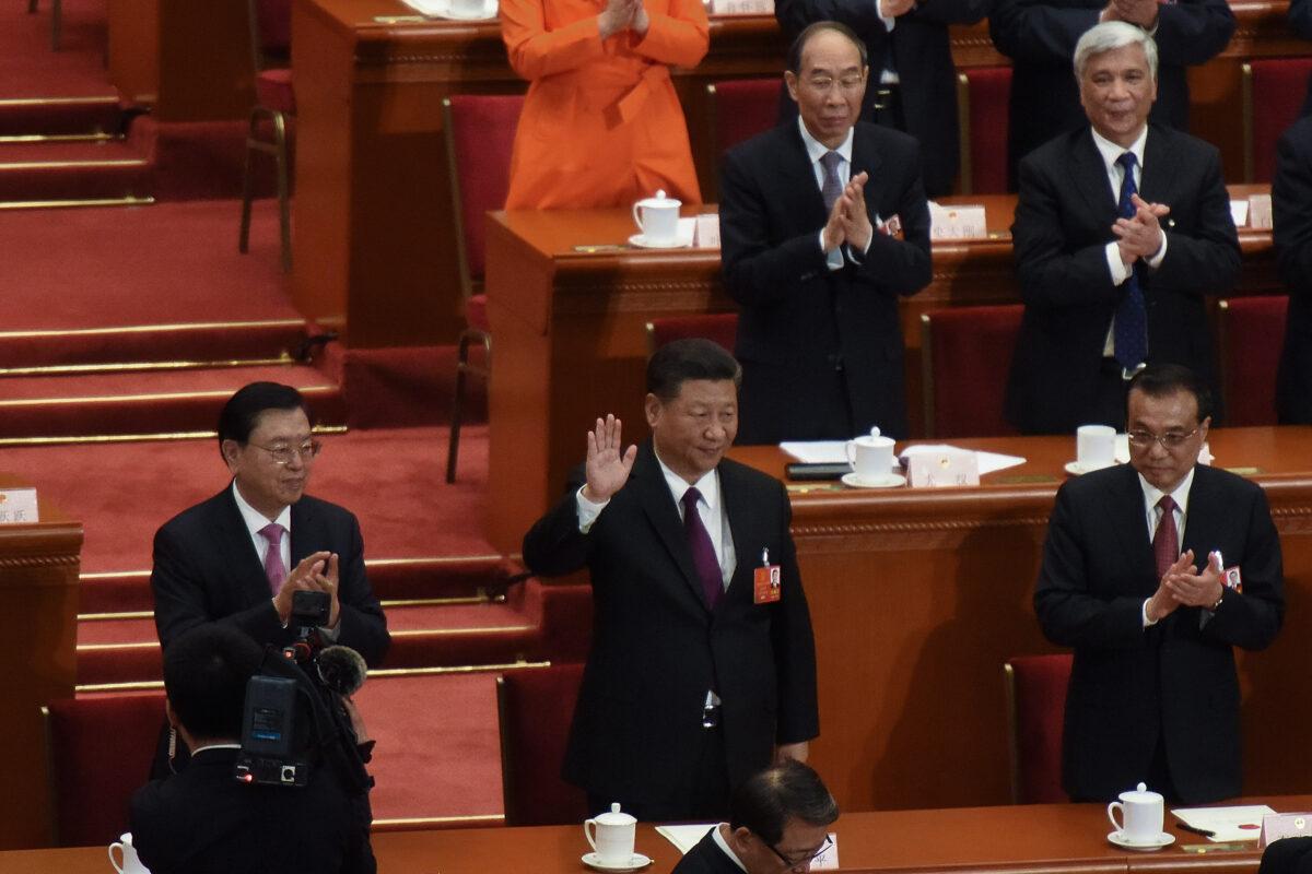 Chinese Communist Party leader Xi Jinping (C) waves to the attendees, with Chinese Premier Li Keqiang (R) and member of the Politburo Standing Committee Li Zhanshu (L) applauding by his side, after being elected for a second five-year term during the fifth plenary session of the first session of the 13th Congress in Beijing, China, on March 17, 2018. (Etienne Oliveau/Getty Images)