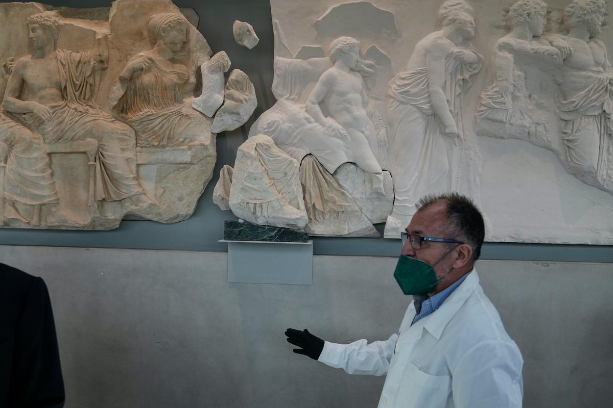 A conservator stands next to a Parthenon fragment, on loan from the Antonino Salinas Regional Archaeological Museum of Palermo, at the Parthenon Gallery of the Acropolis Museum, in Athens, on Jan. 10, 2022. (Thanassis Stavrakis/AP Photo)
