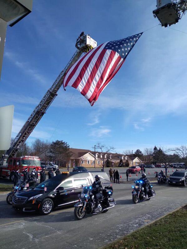 Cleveland police motorcycle officers escort the hearse carrying the casket of Officer Shane Bartek past the fire trucks holding a large American flag following his funeral on Jan. 11, 2022. (Michael Sakal/The Epoch Times)