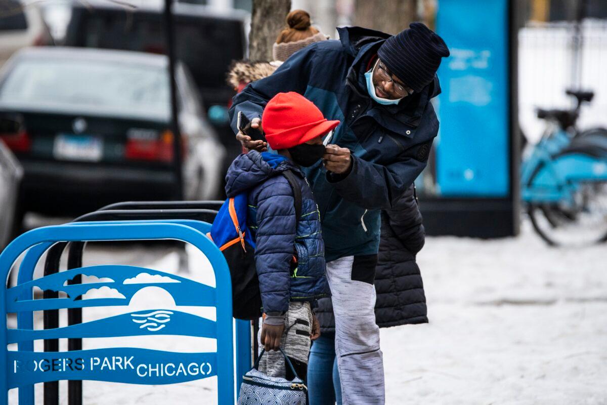 A man adjusts a boy's mask as they arrive at a school in Chicago, Ill., on Jan. 12, 2022. (Ashlee Rezin /Chicago Sun-Times via AP)
