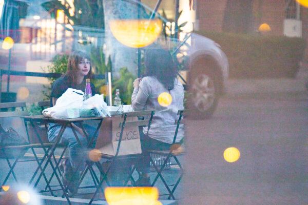 Women reflect off a window while dining outside in Fullerton, Calif., on Dec. 22, 2020. (John Fredricks/The Epoch Times)