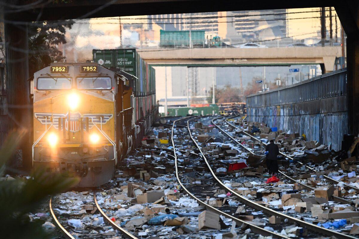 A person carries items collected from the train tracks as a Union Pacific locomotive passes through a section of Union Pacific train tracks littered with thousands of opened boxes and packages stolen from cargo shipping containers, in Los Angeles on Jan. 14, 2022. (Patrick T. Fallon/AFP via Getty Images)