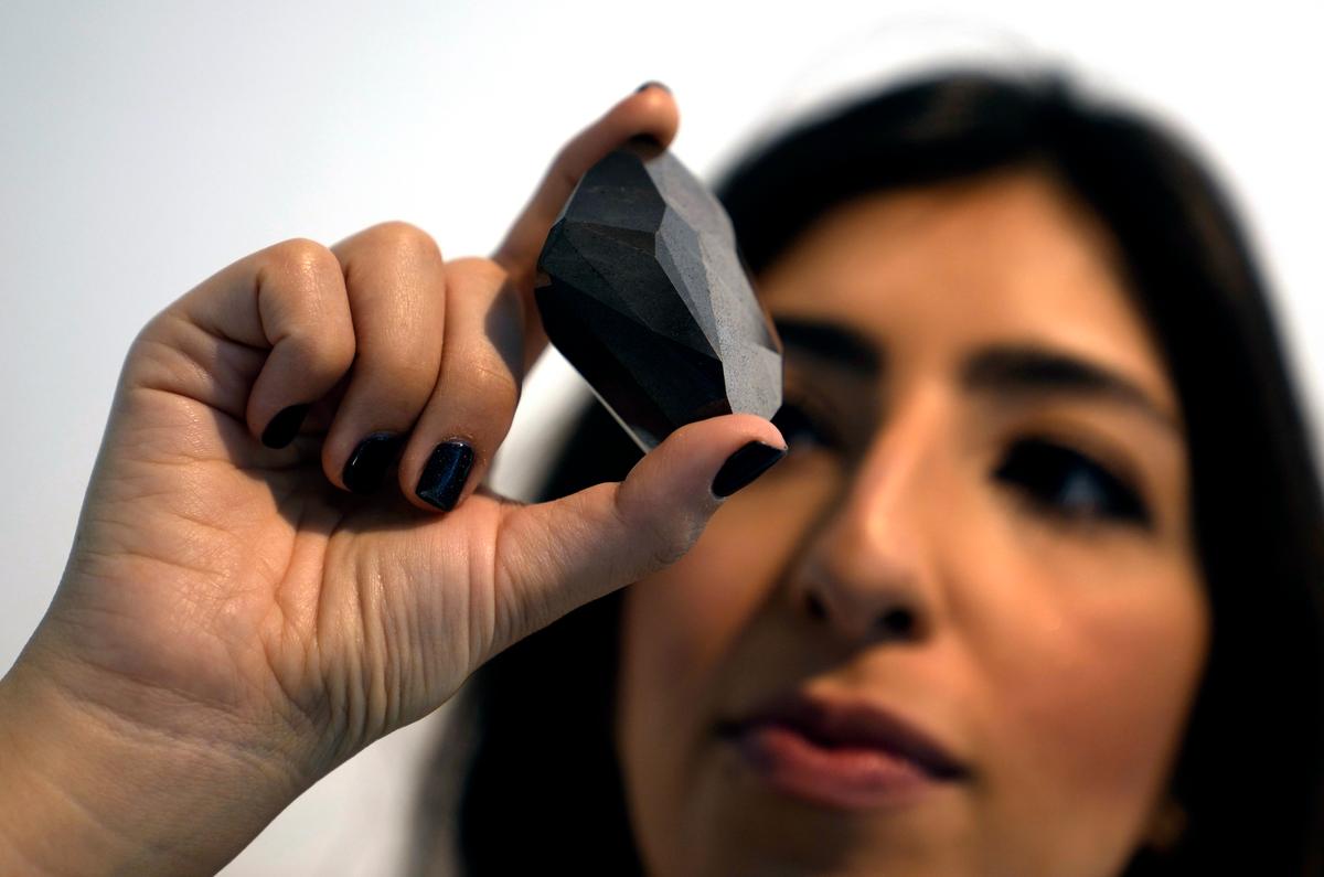 An employee of Sotheby's Dubai presents a 555.55 Carat Black Diamond, “The Enigma,” during the World Unveiling of Major auction highlight at Sotheby's Dubai gallery, in Dubai, United Arab Emirates, on Jan. 17, 2022. (Kamran Jebreili/AP Photo)