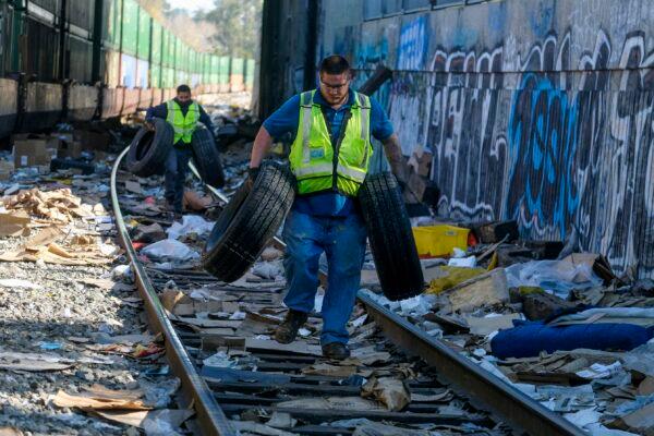 Contract workers Adam Rodriguez (C) and Luis Rosas pick up vehicle tires from among the shredded boxes and packages along a section of the Union Pacific train tracks in downtown Los Angeles on Jan. 14, 2022. (Ringo H.W. Chiu/AP Photo)