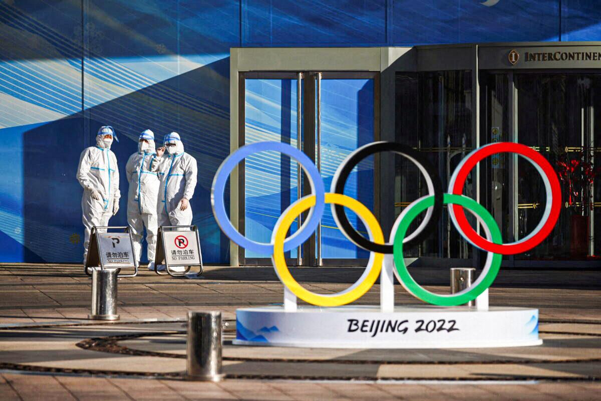 Workers in PPE stand next to the Olympic rings inside the closed-loop area near the National Stadium, or the Bird's Nest, where the opening and closing ceremonies of the Beijing 2022 Winter Olympics will be held, in Beijing on Dec. 30, 2021. (Thomas Peter/Reuters)