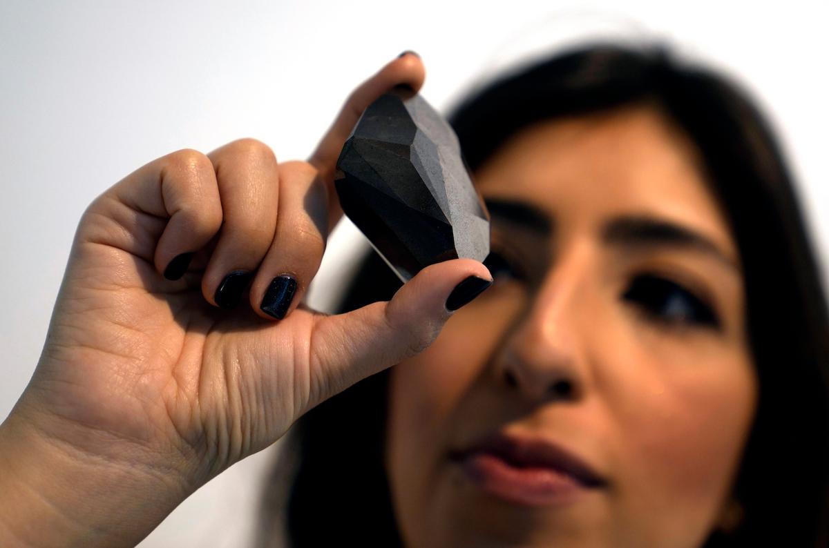 An employee of Sotheby's Dubai presents a 555.55-carat black diamond, “The Enigma,” at Sotheby's Dubai gallery, in Dubai, United Arab Emirates, Monday, Jan. 17, 2022. (Kamran Jebreili/AP Photo)