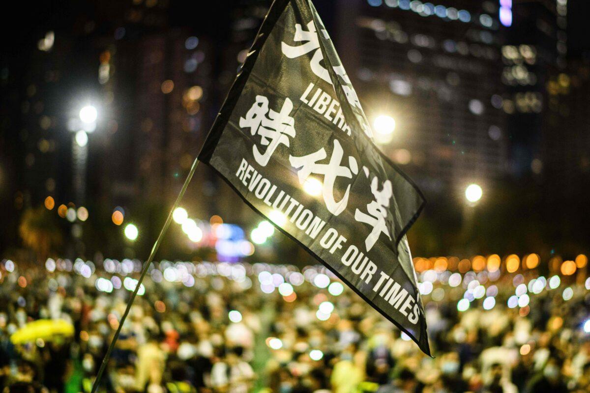 Attendees raise a flag that reads ‘Liberate Hong Kong, Revolution Of Our Times’ during a candlelit remembrance in Victoria Park in Hong Kong on June 4, 2020. (Anthony Wallace/AFP via Getty Images)