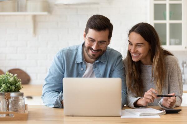 A happy couple watches the computer screen together. (fizkes/Shutterstock)