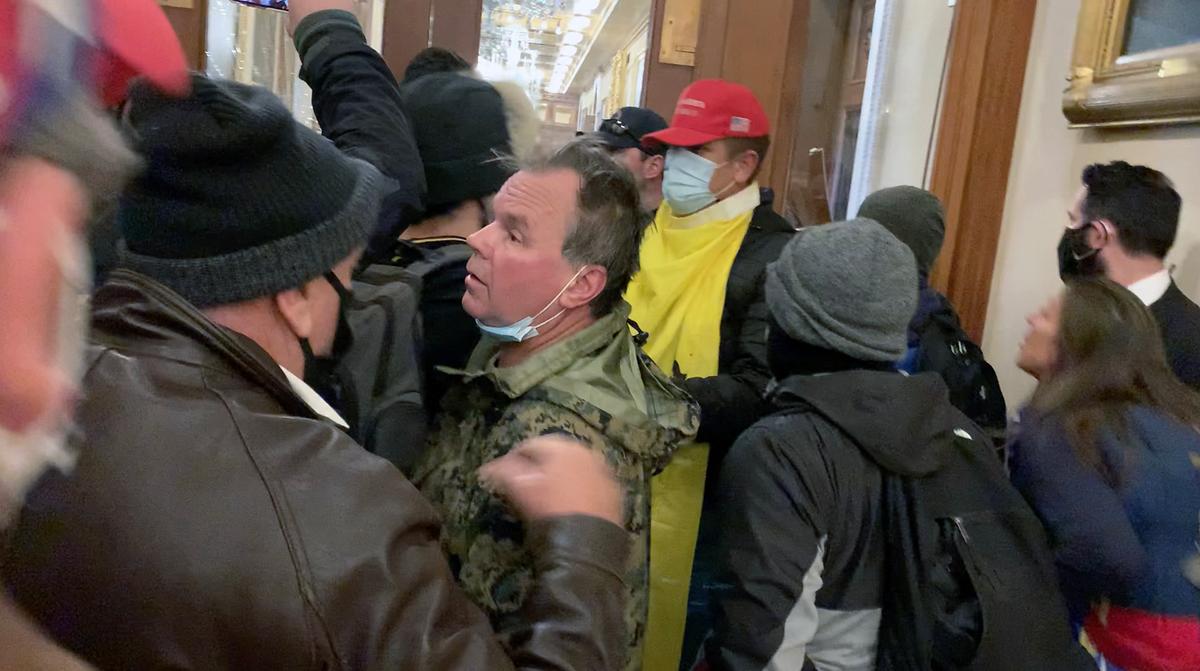 Ashli Babbitt (at right) jumps up and down in frustration while shouting at rioters damaging the windows to the Speaker's Lobby on Jan. 6, 2021. The tall man wearing the yellow Gadsden flag hands a black helmet to rioter Zachary Alam, who uses it to smash windows. (Video Still / Sam Montoya for The Epoch Times)