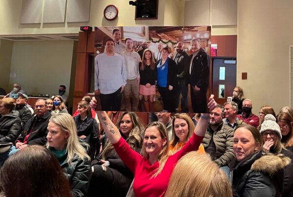 An attendee holds up a board member group photo in which they were all unmasked during the Loudoun County School Board meeting in Ashburn, Va., on Jan. 25, 2022. (Terri Wu/The Epoch Times)