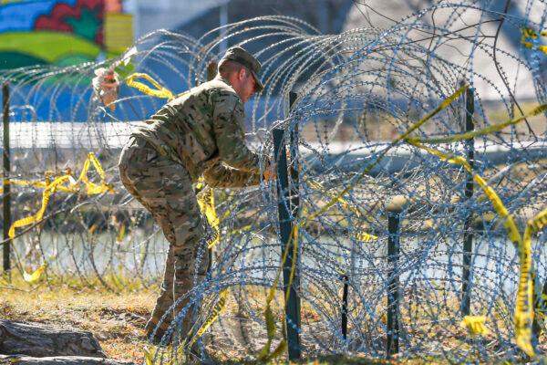 A Texas National Guardsman fixes the razor wire fencing on the bank of the Rio Grande with Mexico on the far side, in Eagle Pass, Texas, on Jan. 25, 2022. (Charlotte Cuthbertson/The Epoch Times)