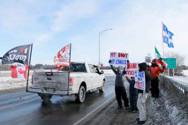 Supporters of the "Freedom Convoy" hold signs as trucks depart an area south of Montreal on Jan. 28, 2022. (Noé Chartier/The Epoch Times)
