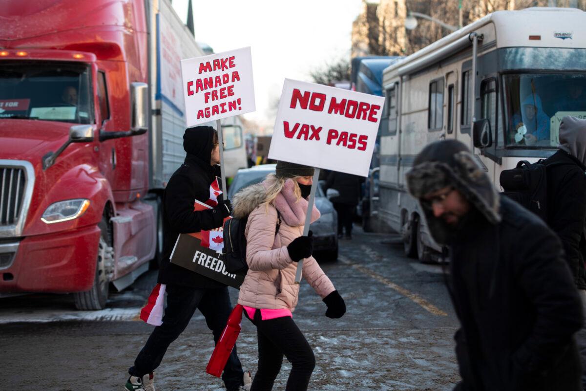 People walk in front of trucks parked on Wellington Street as they join a rally against COVID-19 restrictions on Parliament Hill, in Ottawa, on Jan. 29, 2022. (Justin Tang/The Canadian Press via AP)
