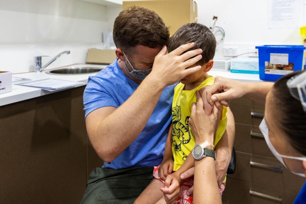 2022年1月11日、オーストラリア・シドニーのバルゴウラで、ファイザーのCOVID-19ワクチンを接種する息子の顔を覆う父親。(ジェニー・エヴァンス/ゲッティイメージズ)