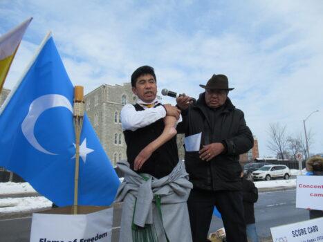 Tibetan activist Tsewang Dhondup (L) shows his permanently damaged arm while speaking at the "Genocide Games" opening ceremony outside the Chinese Embassy in Ottawa on Feb. 4, 2022. (Donna Ho/The Epoch Times)