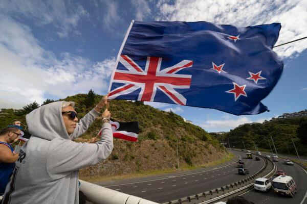 A protester waves an upside down New Zealand flag on an overpass to welcome a protest convoy of trucks and other vehicles into central Wellington, New Zealand, on Feb. 8, 2022. (Marty Melville/AFP via Getty Images)
