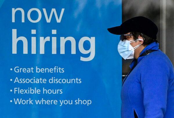 A woman wearing a protective mask walks past a "Now Hiring" sign in front of a store in Arlington, Va., on Jan. 13, 2022. (Olivier Douliery/AFP via Getty Images)