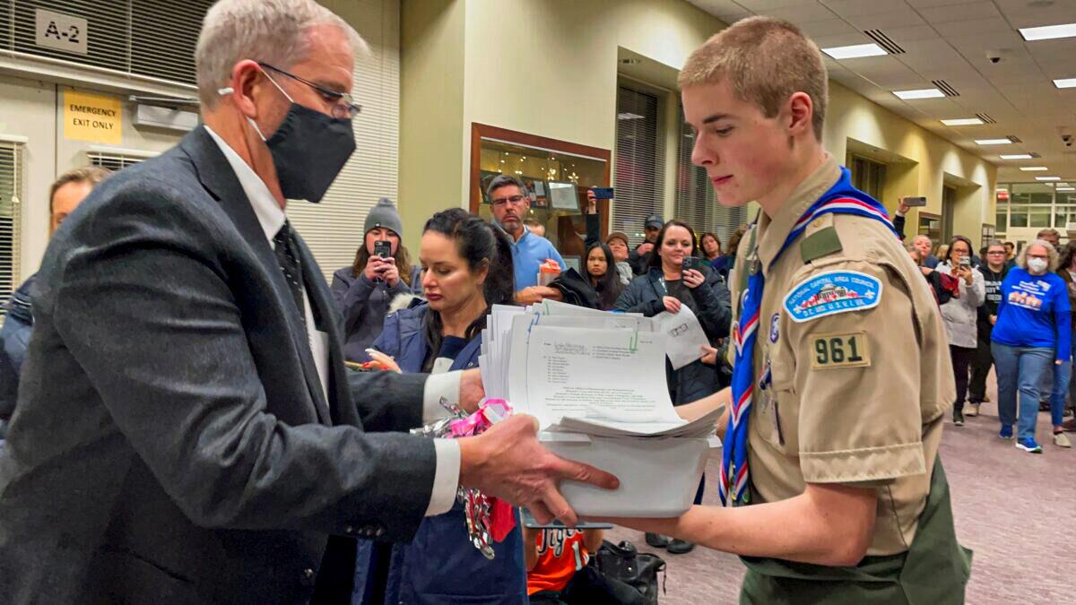 Jarod Missler, 18, a senior at Woodgrove High School and an Eagle Scout, gives one of the nine boxes of notarized affidavits to Loudoun County Public Schools (LCPS) Chief Operations Officer Kevin Lewis at the LCPS administration building in Ashburn, Va., on Feb. 8, 2022. (Terri Wu/The Epoch Times)