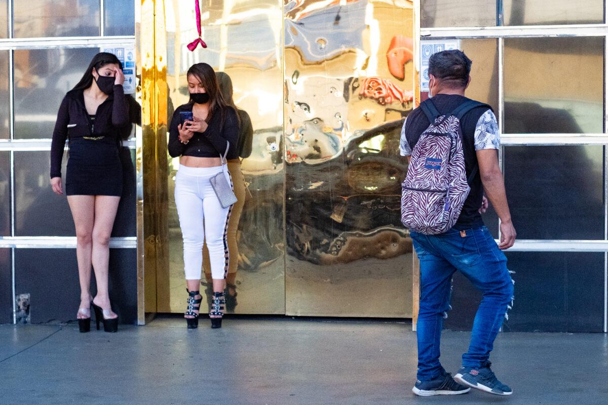 A man walks by two women standing near a strip club in Zona Norte, Tijuana, Mexico, on Jan 16, 2021. (John Fredricks/The Epoch Times)