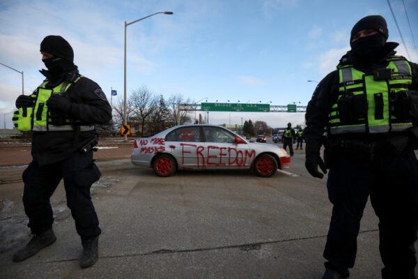 Police officers stand guard in front of a car painted with slogans as truckers and supporters continue blocking access to the Ambassador Bridge, which connects Detroit and Windsor, in protest against COVID-19 mandates and restrictions, in Windsor, Ont., on Feb. 12, 2022. (Reuters/Carlos Osorio)