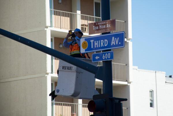 A worker unveils the honorary street sign Tom Hom Avenue, upon Mayor Todd Gloria’s announcement in downtown San Diego on Feb. 12, 2022. (Jane Yang/The Epoch Times)