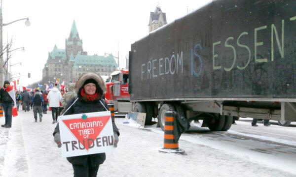 A protester holds a sign as she walks on Wellington St. in Ottawa on Feb. 12, 2022. (Noé Chartier/The Epoch Times)