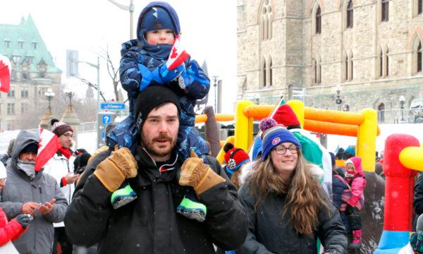 A young family walks through the protest on Wellington St. in Ottawa on Feb. 12, 2022. (Noé Chartier/The Epoch Times)