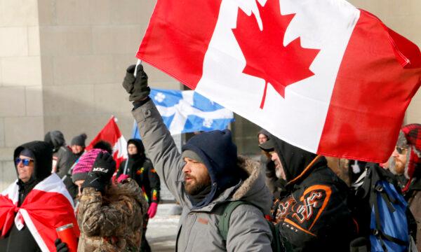 A man holds a Canadian flag as he walks up Wellington St. in Ottawa on Feb. 12, 2022. (Noé Chartier/The Epoch Times)