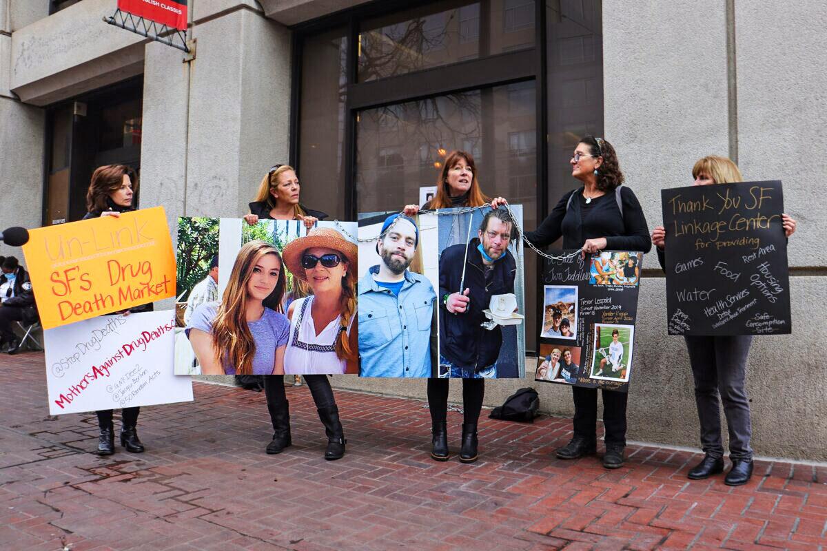 Members of Mothers Against Drug Deaths hold a chain of posters in front of the Tenderloin Linkage Center in San Francisco on Feb. 5, 2022. (Cynthia Cai/The Epoch Times)