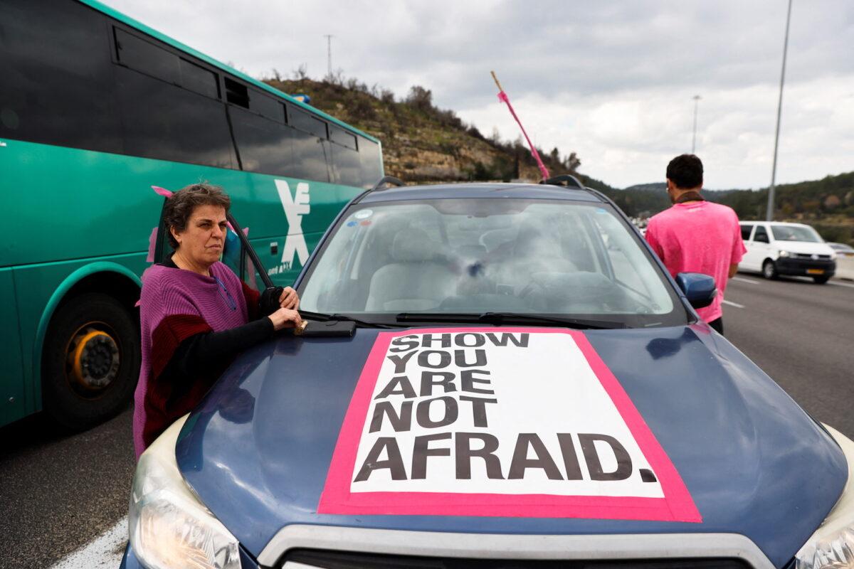 A protestor stands next to her car as she takes part in an Israeli "Freedom Convoy" heading to Jerusalem to protest against COVID-19 restrictions, in Shoresh, near Jerusalem, on Feb. 14, 2022. (Amir Cohen/Reuters)