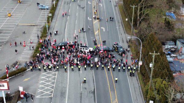 Protesters rally near the Pacific Highway border crossing while police keep watch, in Surrey, B.C., on Feb. 13, 2022. (Chris Ivany)