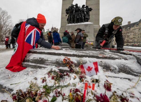 Veterans clear snow and ice off the Tomb of the Unknown Soldier as protests against COVID-19 restrictions happen on Parliament Hill in Ottawa on Feb. 12, 2022. (The Canadian Press/Frank Gunn)
